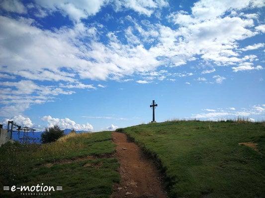 Kreuz auf grünem Hügel unter blauem Himmel mit Wolken