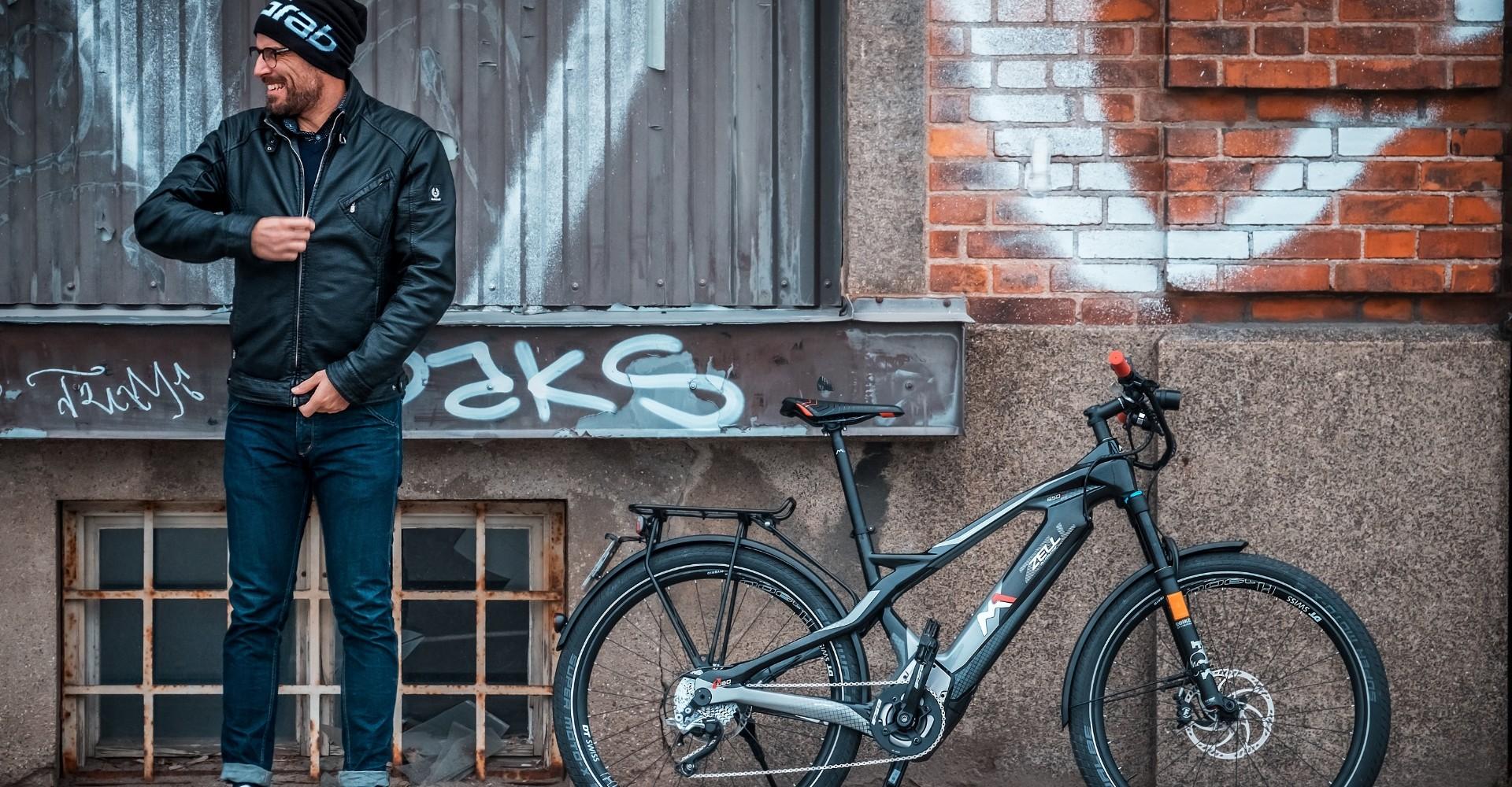 Mann mit M1 Zell e-Bike vor einer Wand