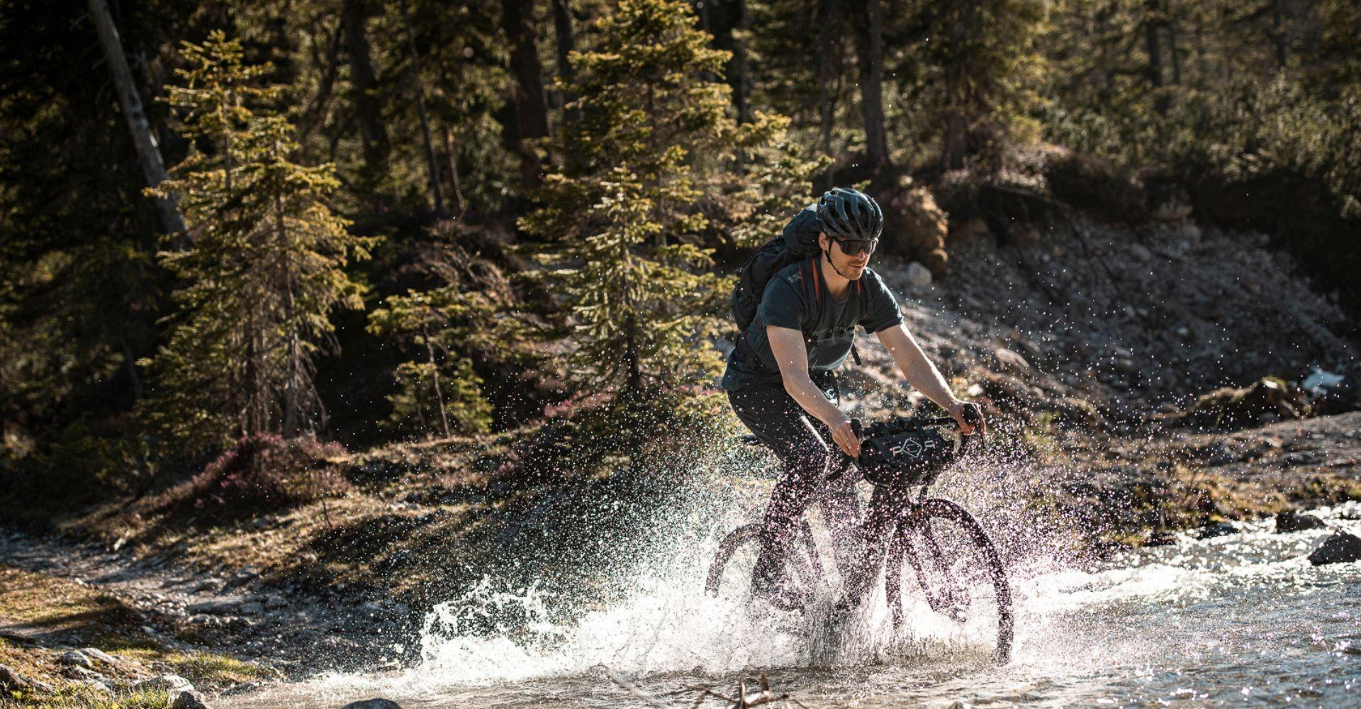 Mann fÀhrt mit Gravel e-Bike durch das Wasser