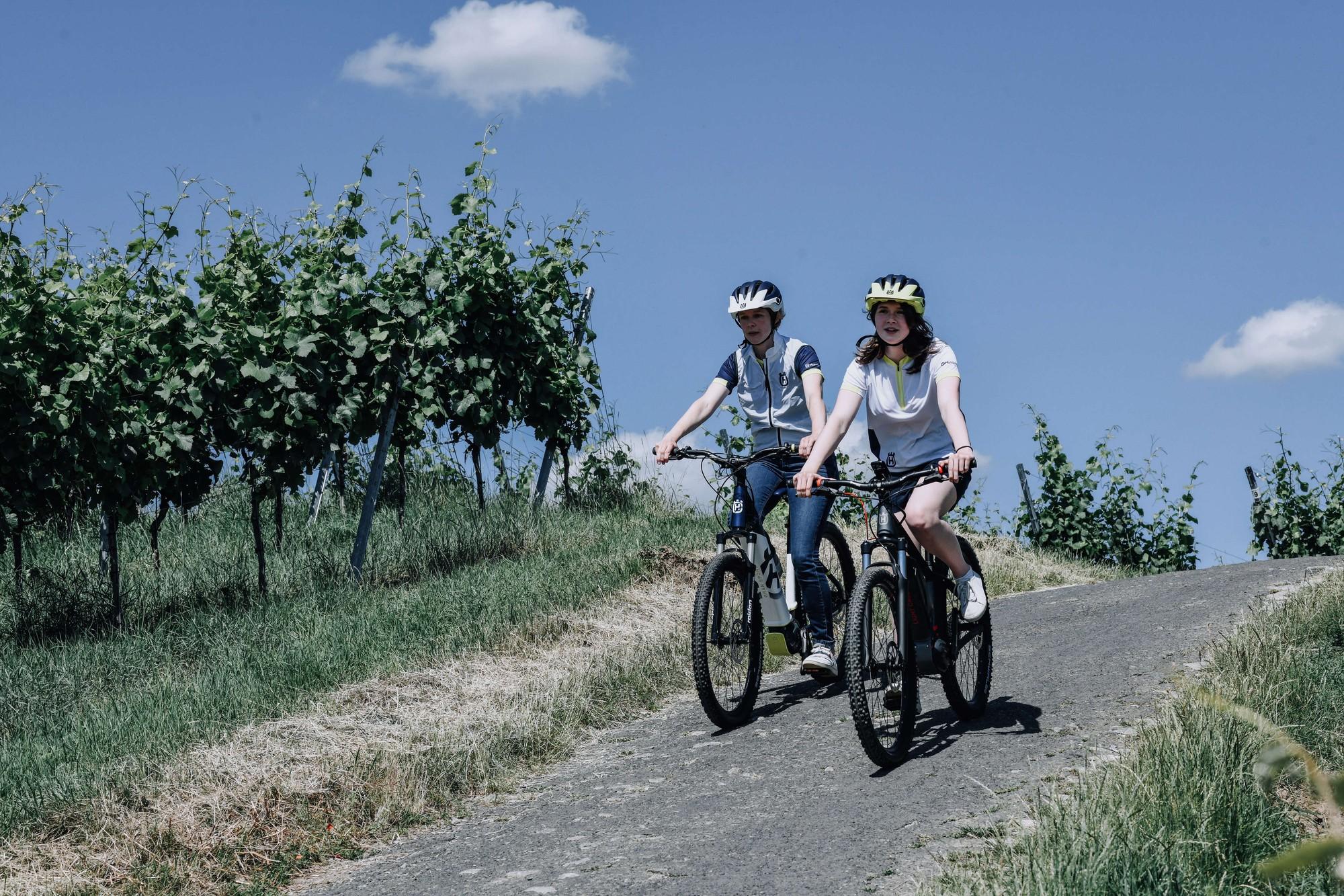 Zwei Jugendliche fahren mit Husqvarna e-Bikes durch sonnige Weinberge.