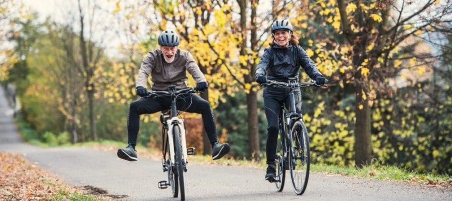 Senioren auf E-Bikes fahren lächelnd im Herbst durch den Park
