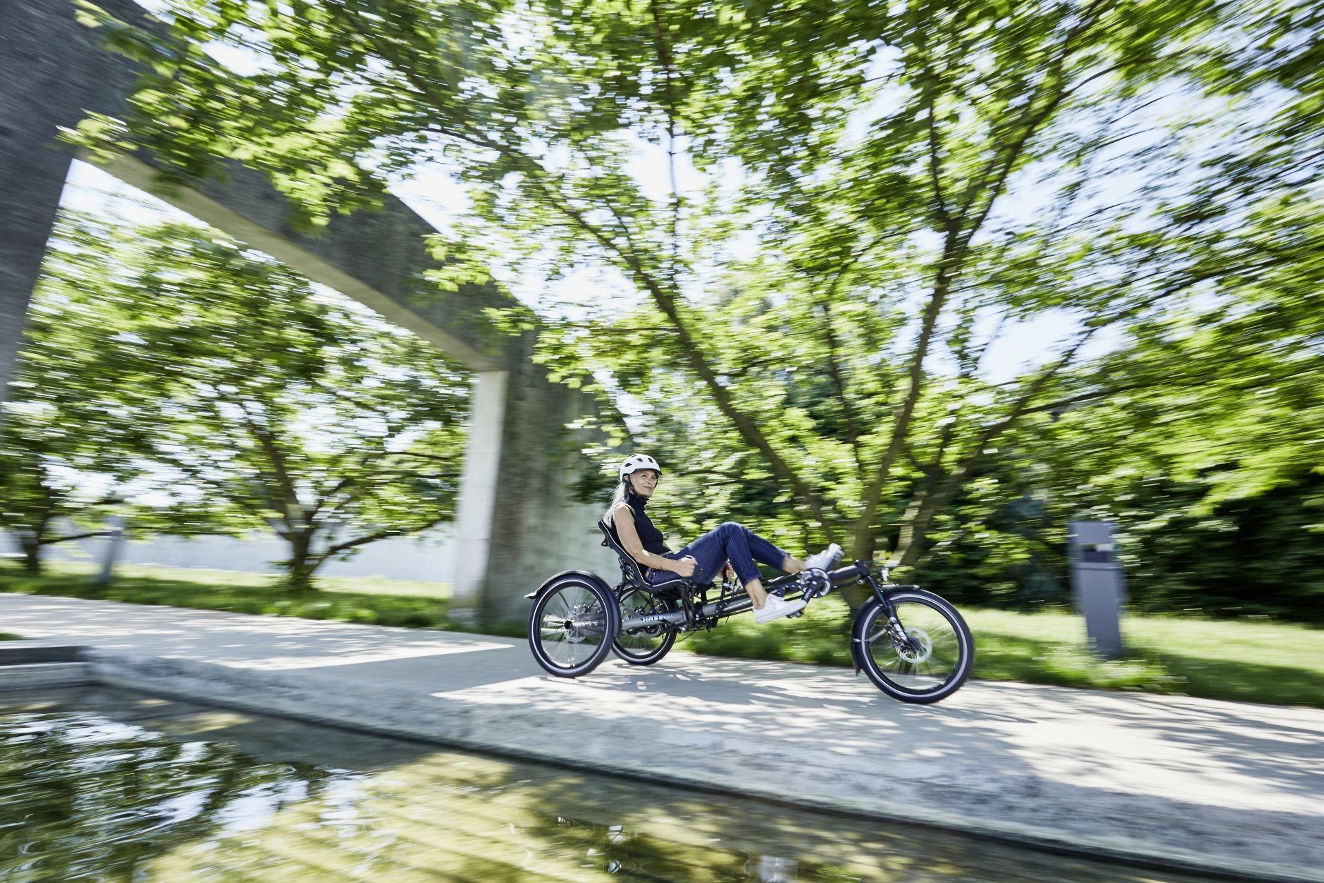 Eine Frau fährt mit einem HASE BIKES Dreirad einen Weg entlang