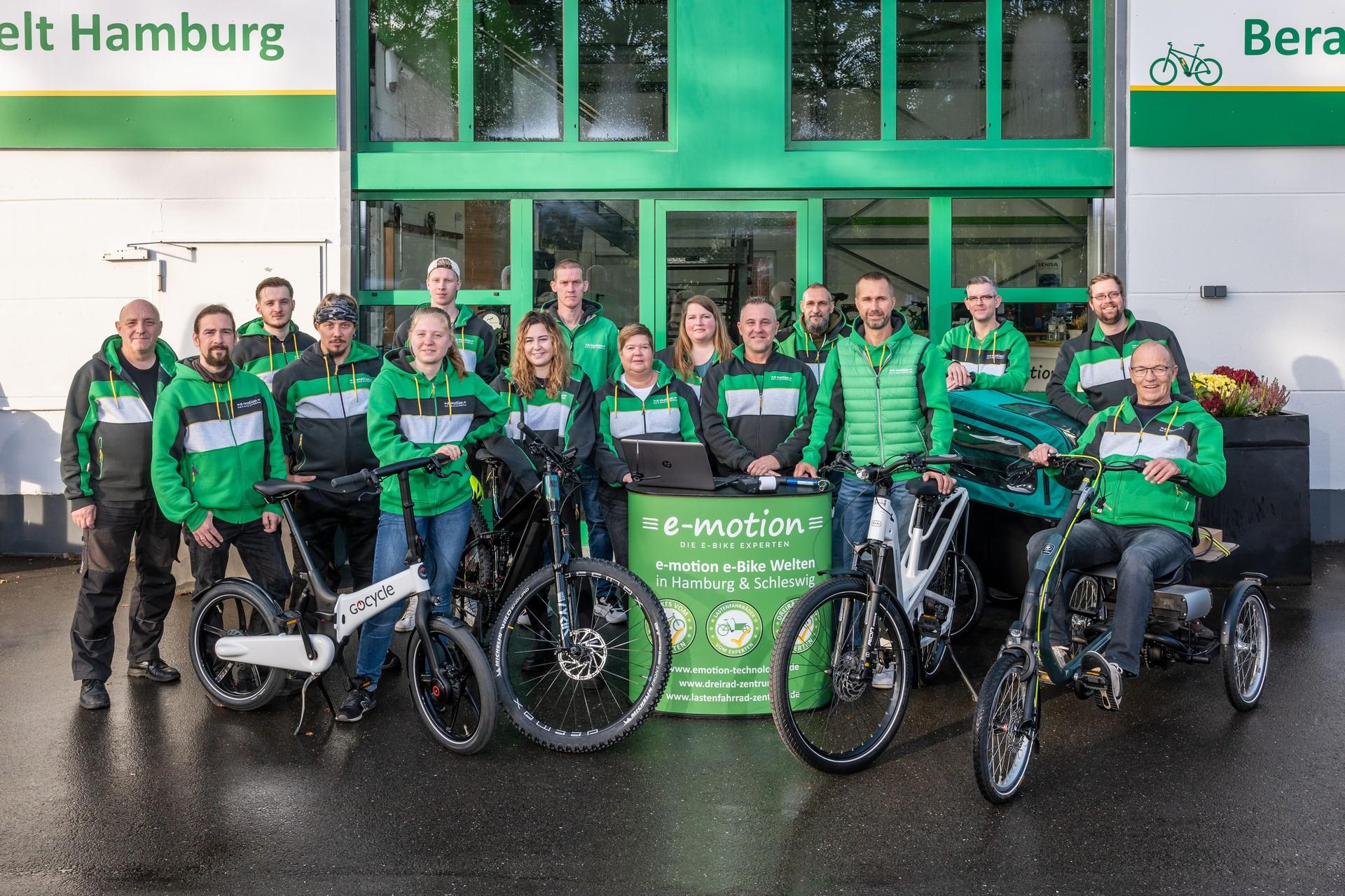 Das Bild zeigt das Team von e-motion Hamburg in grüner Jacken gekleidet und umgeben von verschiedenen e-Bikes.