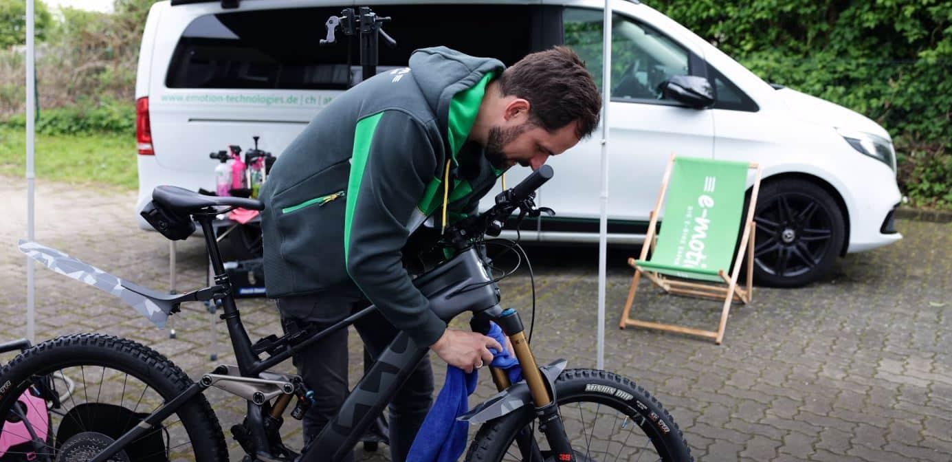 Ein Mann reinigt ein e-Bike vor einem Auto