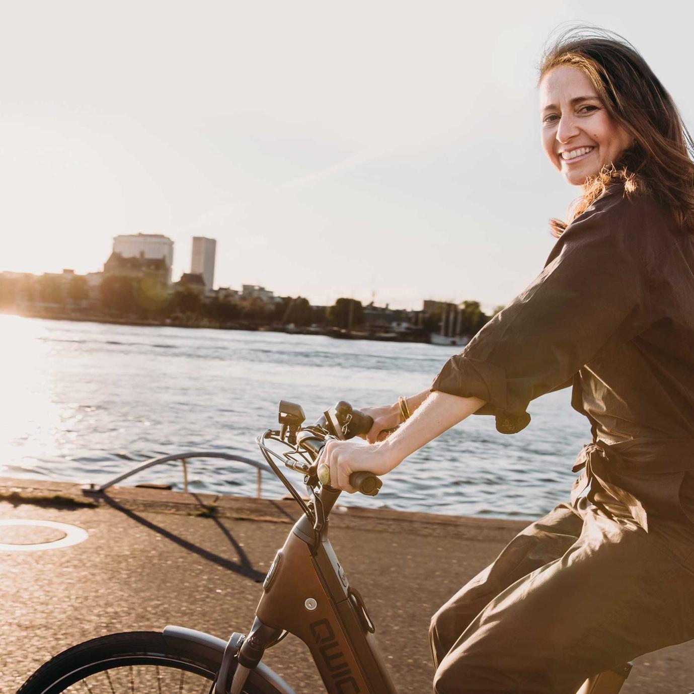 Eine Frau fährt auf dem QWIC Mira e-Bike am Wasser entlang
