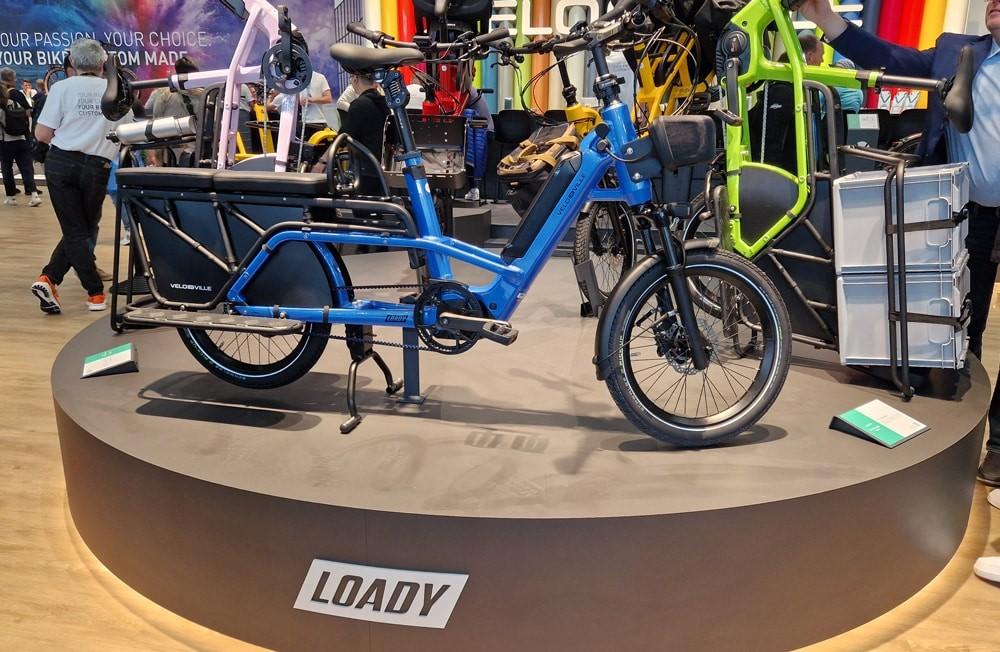 Velo de Ville LOADY e-Bike in Blau mit stabilem Rahmen und Gepäckträger, präsentiert auf runder Plattform.