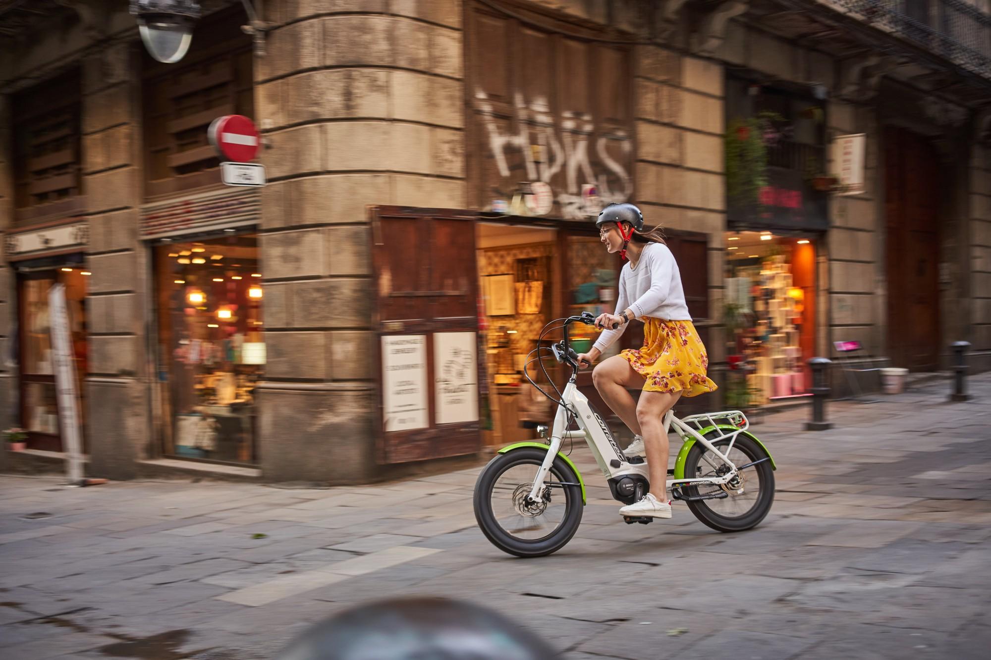 Eine Frau fährt auf einem Corratec LifeS e-Bike durch Barcelona, umgeben von urbaner Architektur und Geschäften.