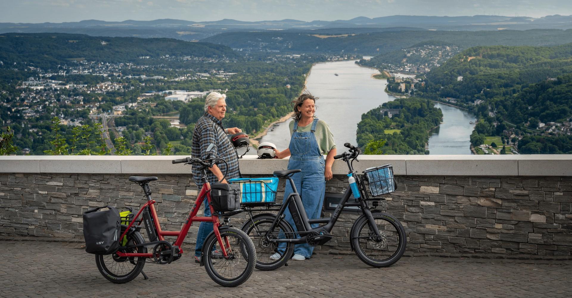 Zwei Personen stehen auf einer Brücke und haben zwei i:SY e-Bikes dabei