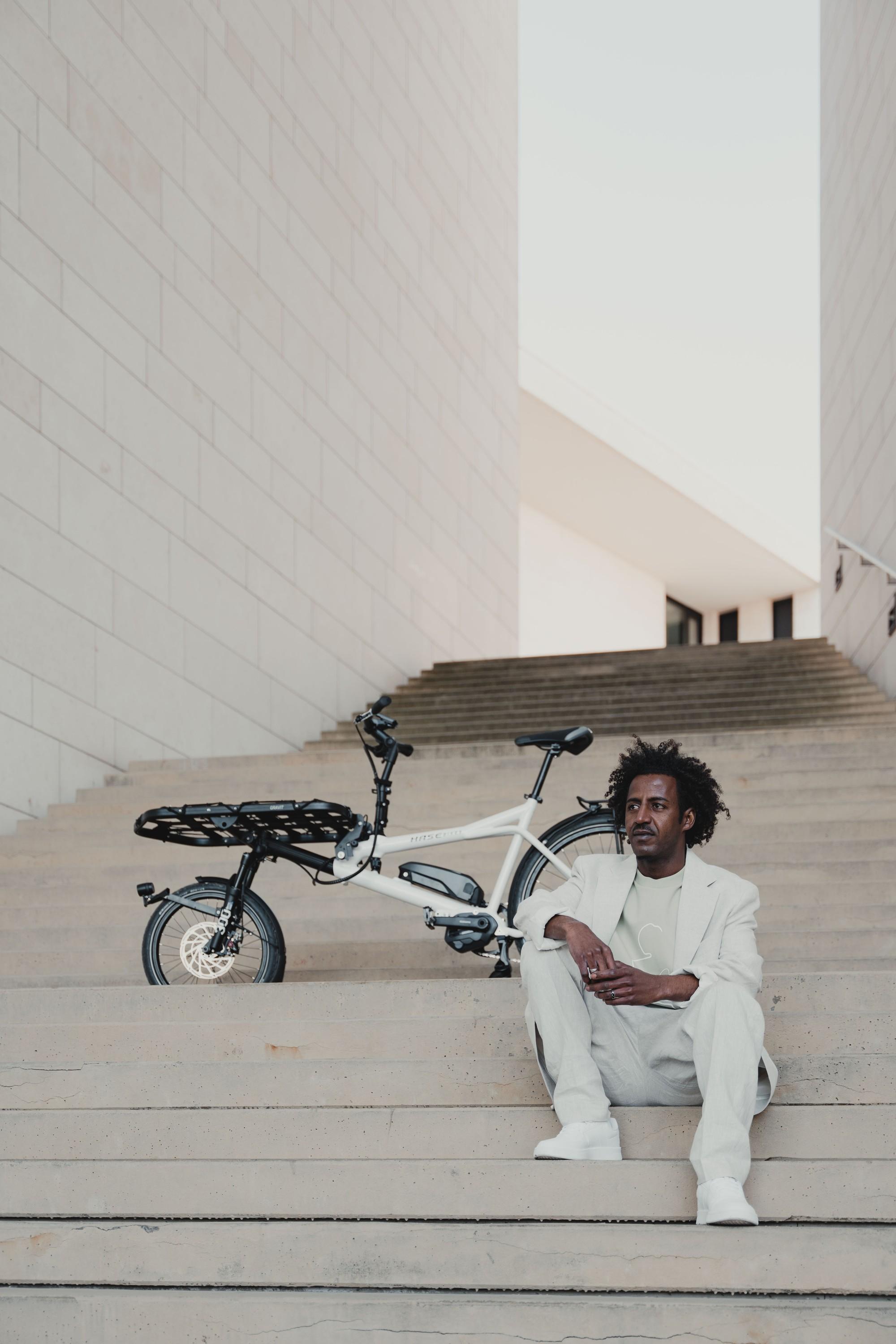 Ein Junger Mann sitzt mit seinem Hase City e-Bike auf einer Treppe in Berlin Mitte.