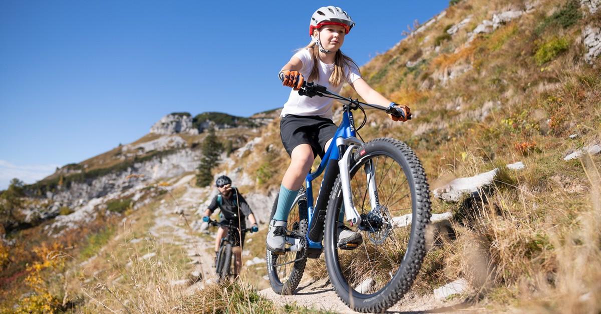 Das Bild zeigt zwei junge Radfahrer, die mit einem Woom E-Bike in einem bergigen Gelände fahren.