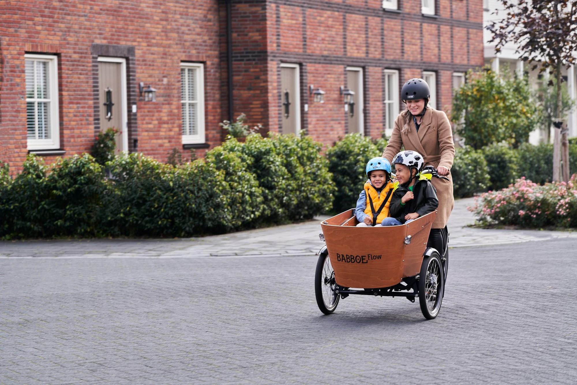 Eine Frau fährt mit dem Babboe Flow und zwei Kindern in der Transportbox über die Straße
