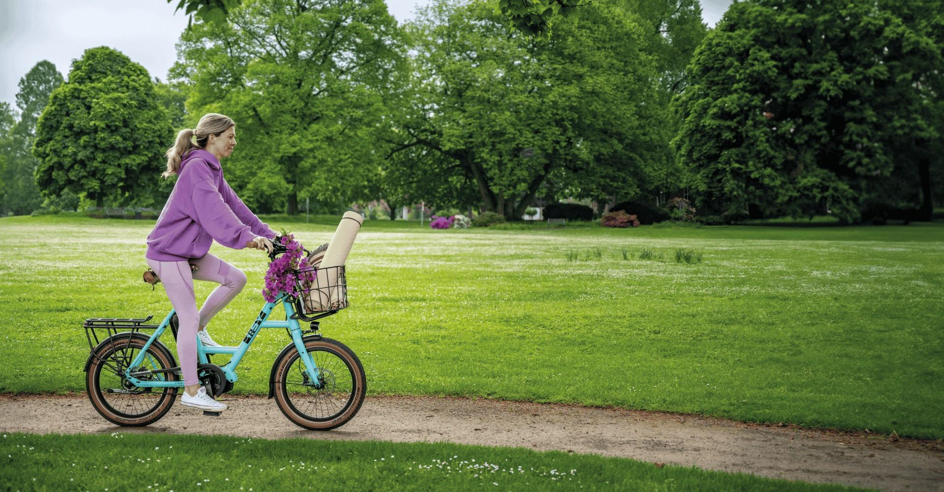 Frau fährt mit dem i:SY e-Bike im Frühling an grüner Wiese vorbei