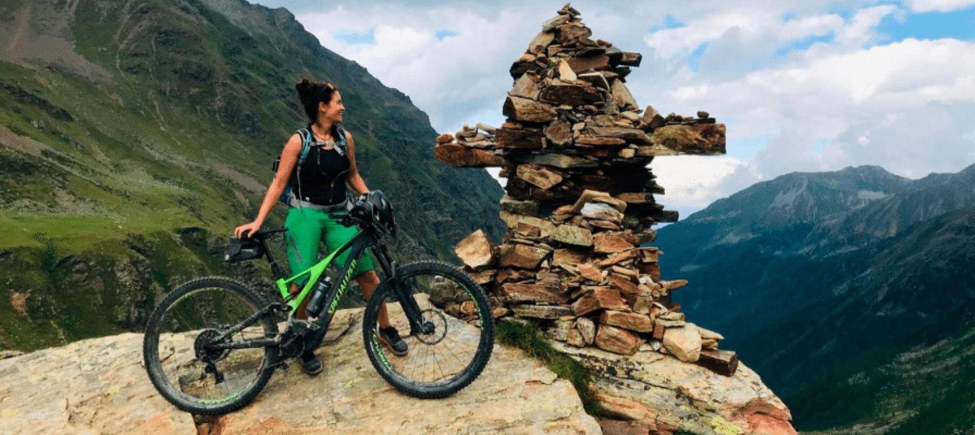 Das Bild zeigt eine Berglandschaft, in der eine Frau mit einem Specialized e-Bike steht.