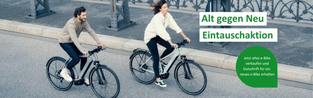 Das Bild zeigt zwei Radfahrer, die fröhlich auf einem modernen Radweg fahren. Der Mann nutzt ein klassisches Fahrra