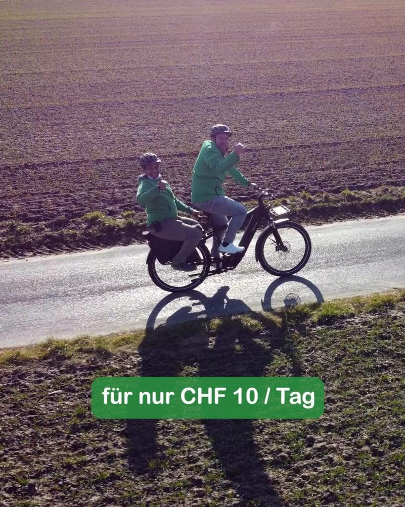 Zwei Personen auf E-Bike auf ländlicher Straße mit Werbetext