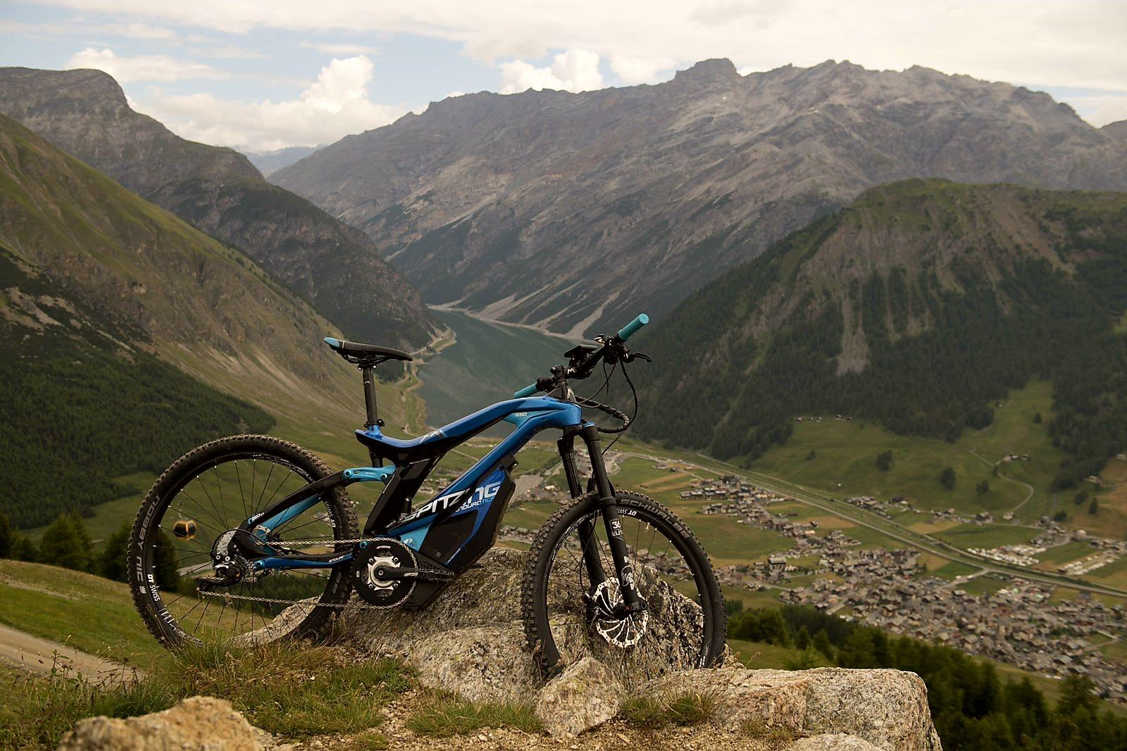 Das Bild zeigt ein E-Bike des Modells M1 Spitzing, das auf einem Felsen in einer beeindruckenden alpinen Landschaft