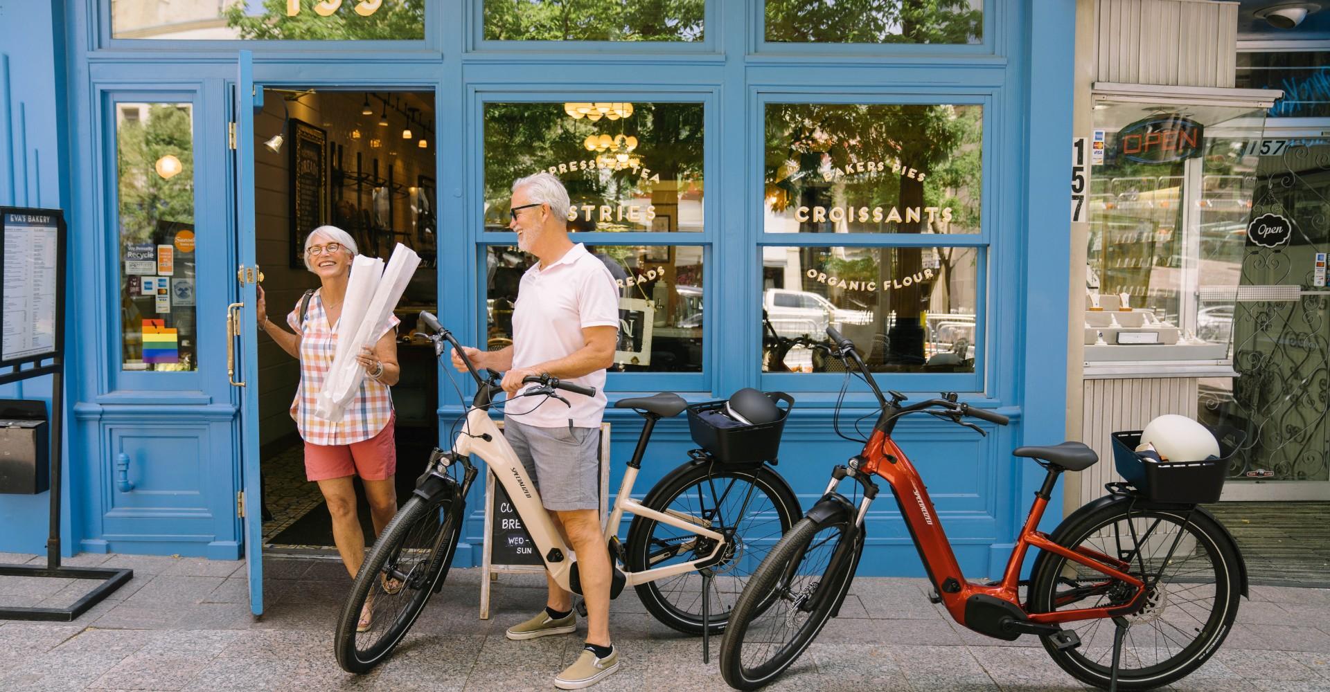 Ein älteres Ehepaar macht eine e-Bike Tour und steht gerade vor einem Geschäft.
