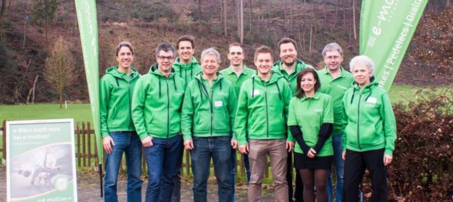 Gruppe in grünen Jacken vor Wald mit e-motion Banner