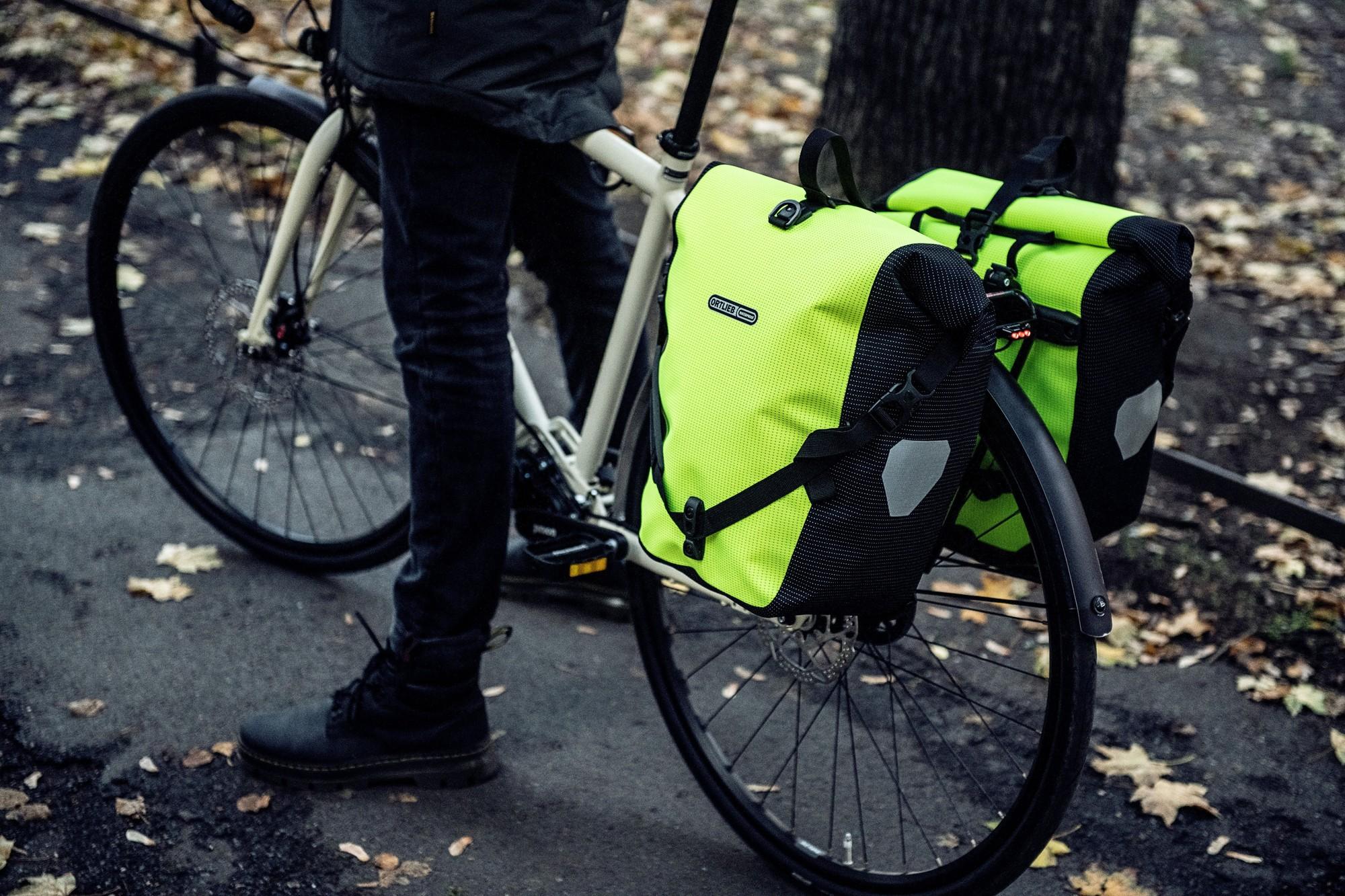 Das Bild zeigt ein Fahrrad, das mit zwei auffälligen, leuchtend Ortlieb Back Roller HV Taschen ausgestattet ist.