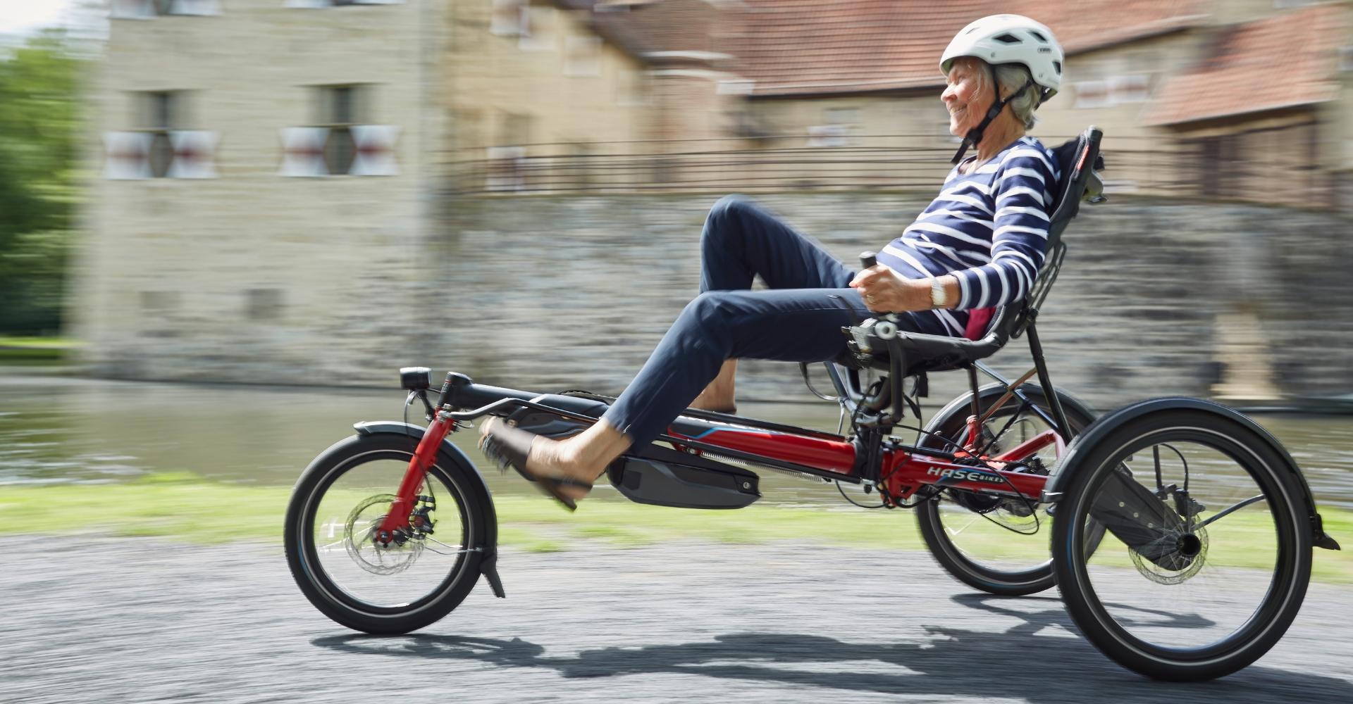 Eine Frau sitzt auf einem HASE BIKE während sie an einer Burg vorbei fährt