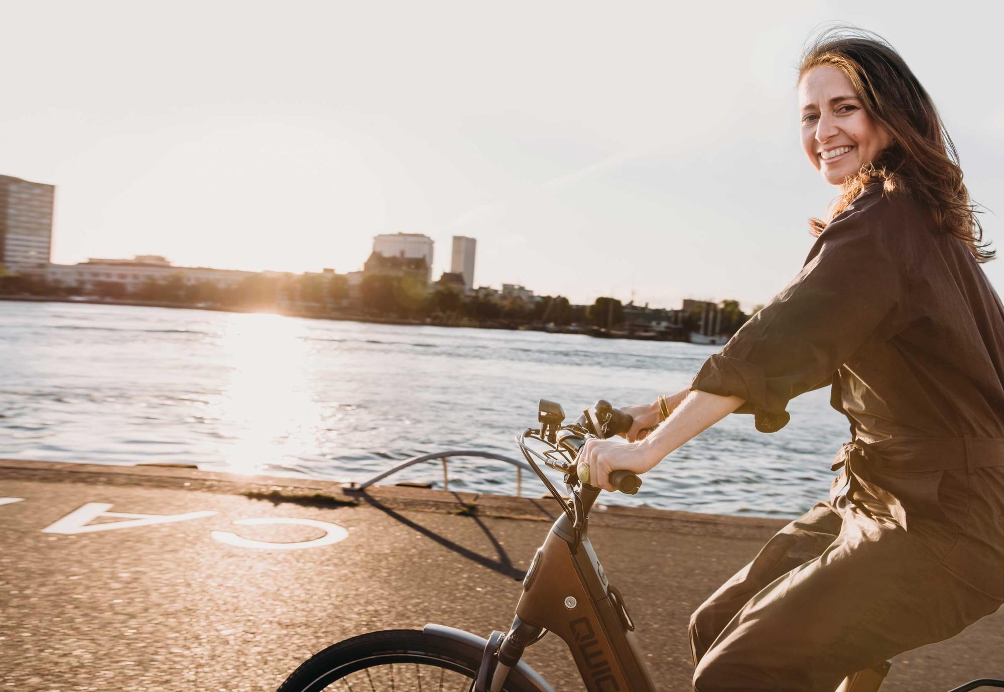 Eine Frau fährt auf dem QWIC Mira e-Bike am Wasser entlang