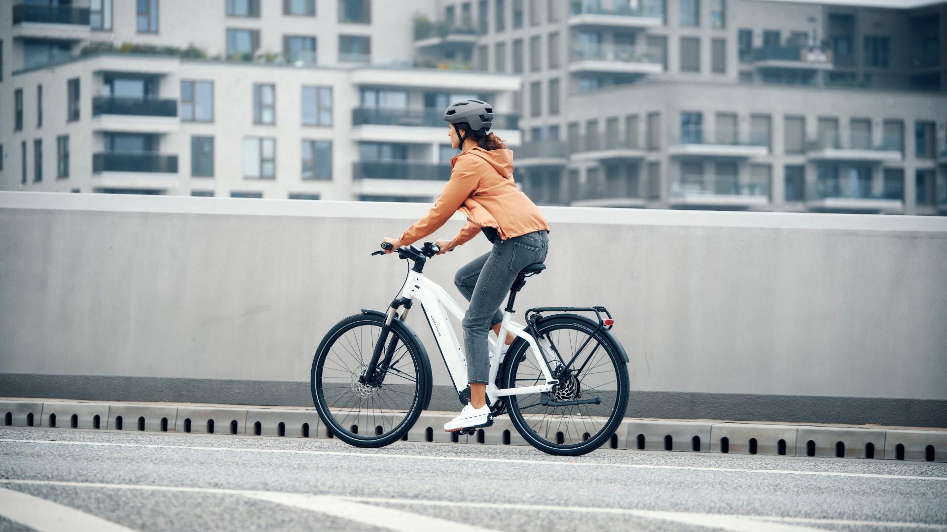 Fahrerin auf einem Riese & Müller E-Bike fährt vor einer modernen Neubau-Skyline. Ideal für urbane Mobilität und st