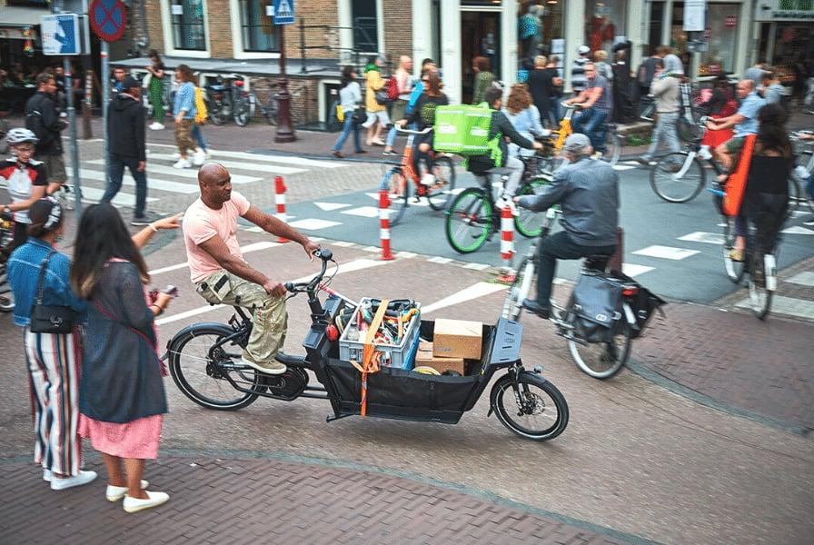 Mann fährt Lastenrad mit Paketen in belebter Stadtstraße