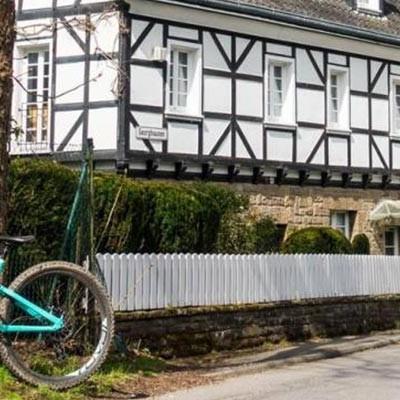 Ein Mountainbike lehnt an einem Baum vor einem idyllischen Fachwerkhaus in Wuppertal. Perfekt für Ausflüge durch di