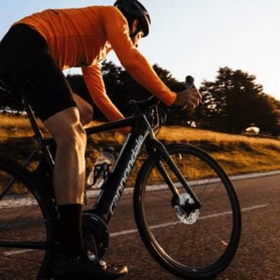 Rennradfahrer bei Sonnenuntergang auf leerer Landstraße