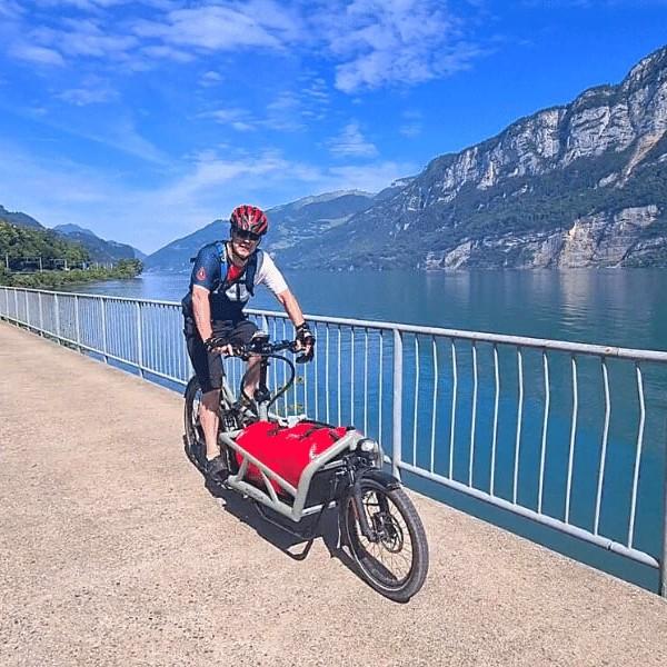 Mann auf E-Bike mit Anhänger fährt entlang eines Sees