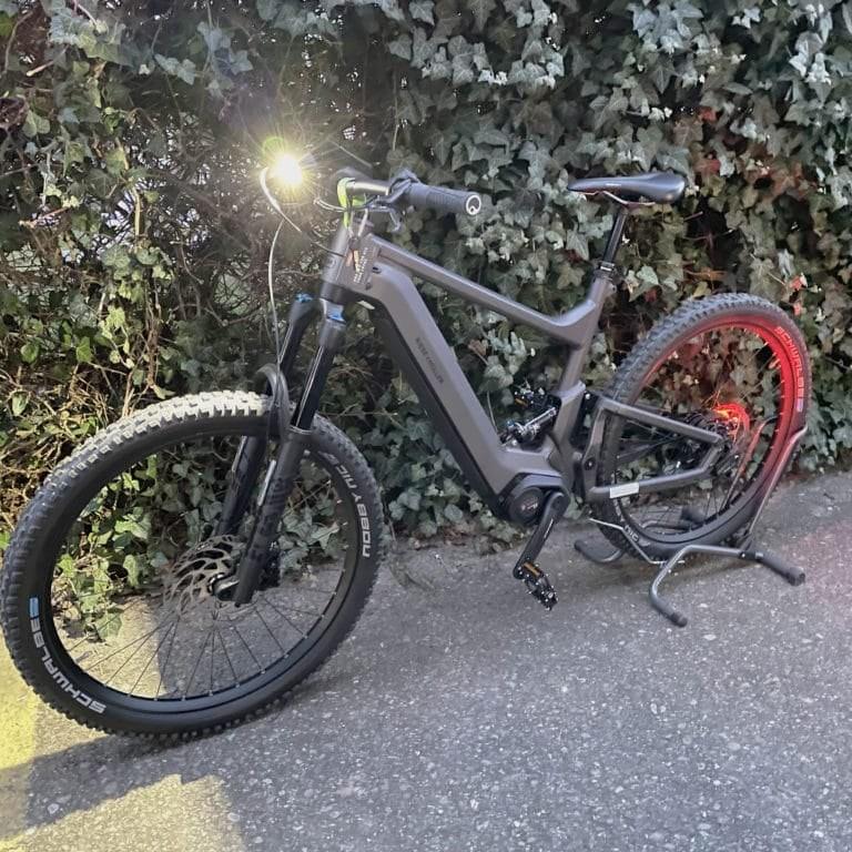 E-Bike mit eingeschaltetem Front- und Rücklicht auf Asphaltweg vor Hecke