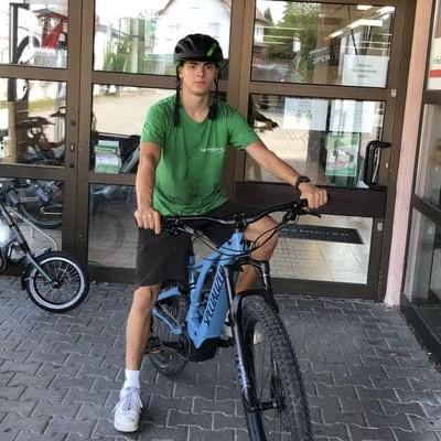 Junger Mann mit Helm auf E-Bike vor Geschäftseingang