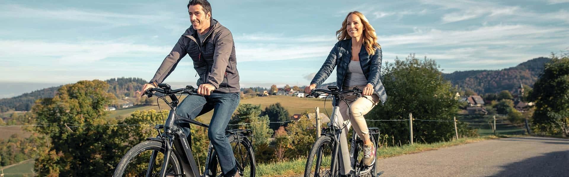 Ein Ehepaar ist mit seinem beiden e-Bikes bei einer Radtour unterwegs im Grünen.