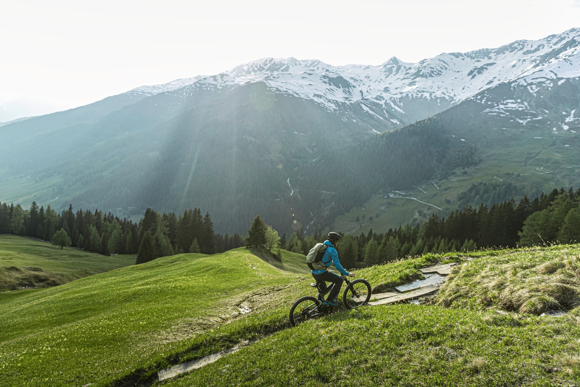 Eine Person fährt mit dem e-MTB Riese & Müller Superdelite durch das Grüne und die Berge