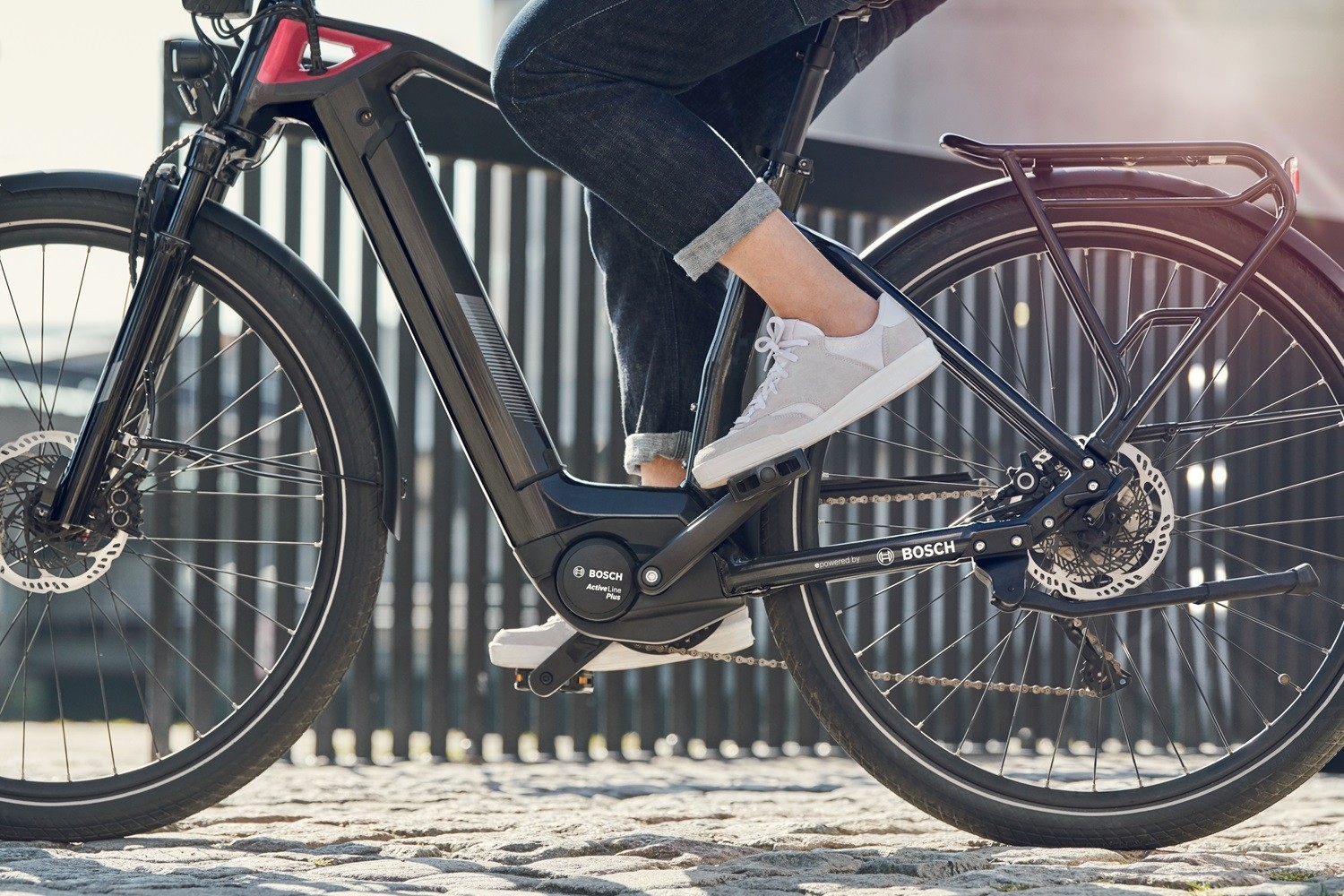 e-Bike mit Bosch Active Line Plus Antrieb, Motor und Rahmen im Fokus, Fahrer mit grauen Sneakern im urbanen Umfeld.