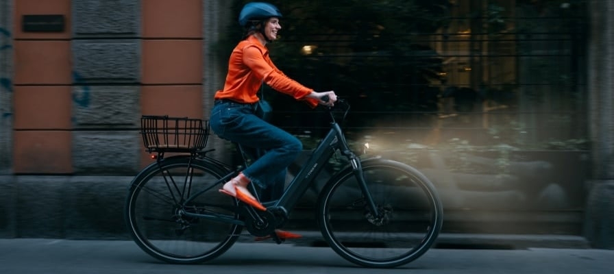 ine Frau in oranger Kleidung fährt ein Bianchi T-Tronik E-Bike auf einer städtischen Straße bei Nacht.