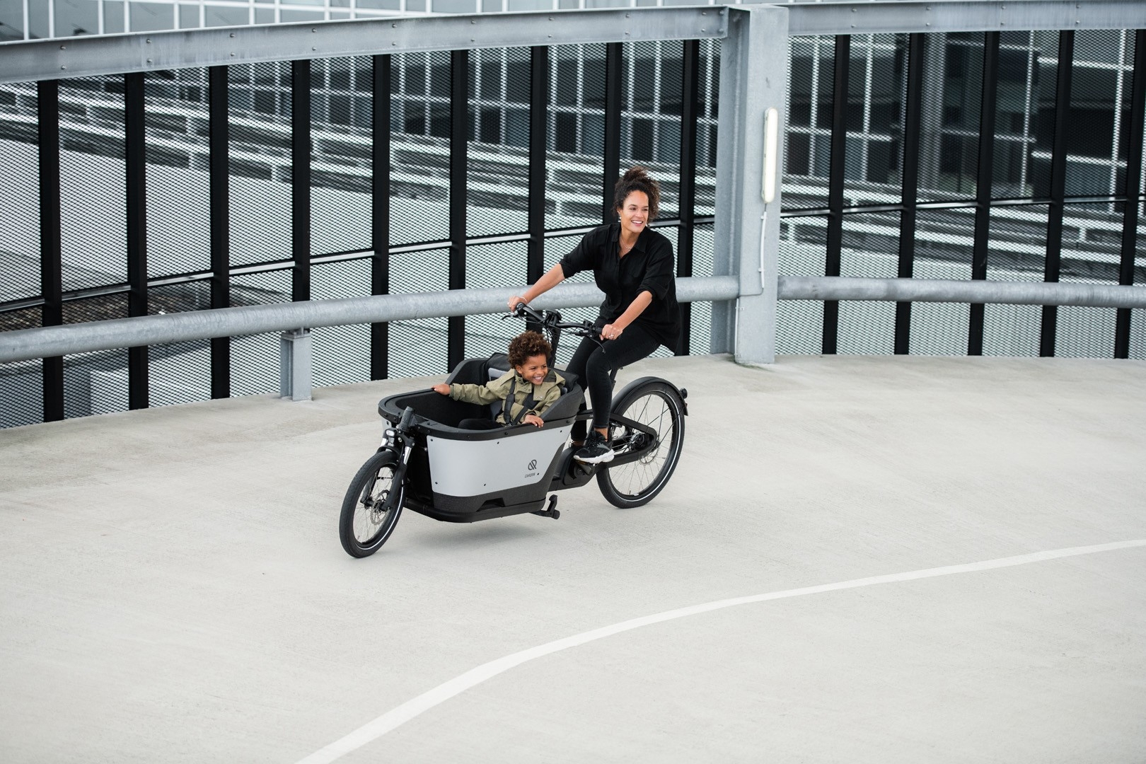 Eine Frau ist mit ihrem Sohn im Carqon Cruiser Lasten e-Bike unterwegs zu einem Spielplatz in Köln.