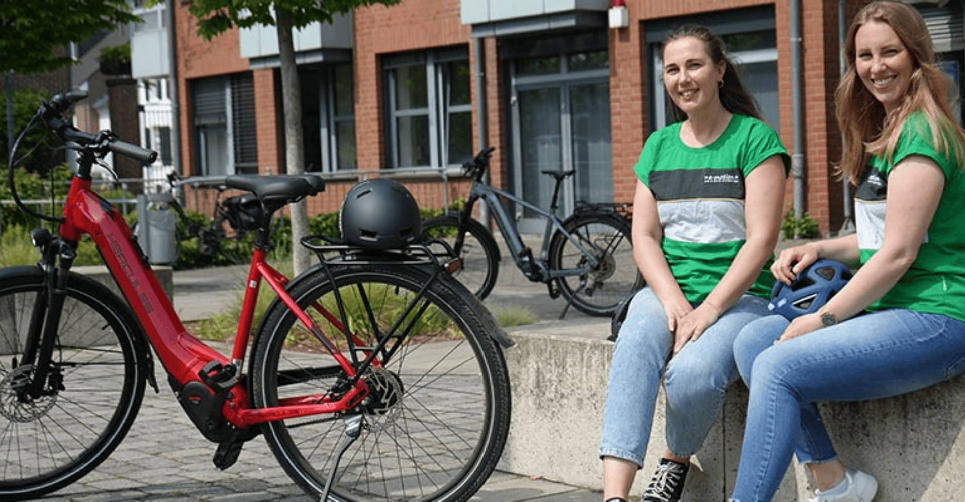Zwei Frau sitzen mit einem Hercules e-Bike auf einer Steinmauer