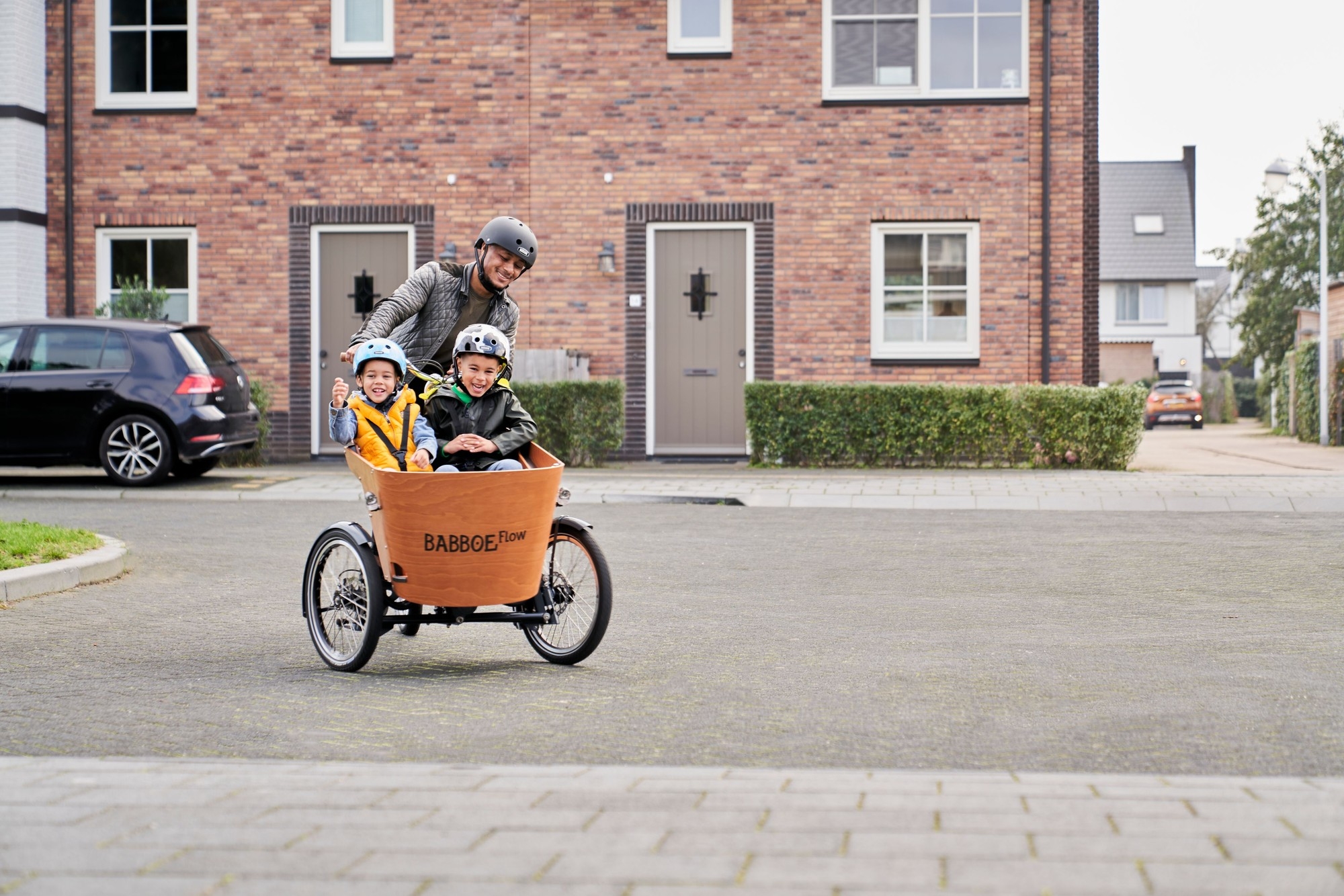 Ein Vater startet gerade mit seinen zwei Kindern im Lasten e-Bike von Zuhaue aus.