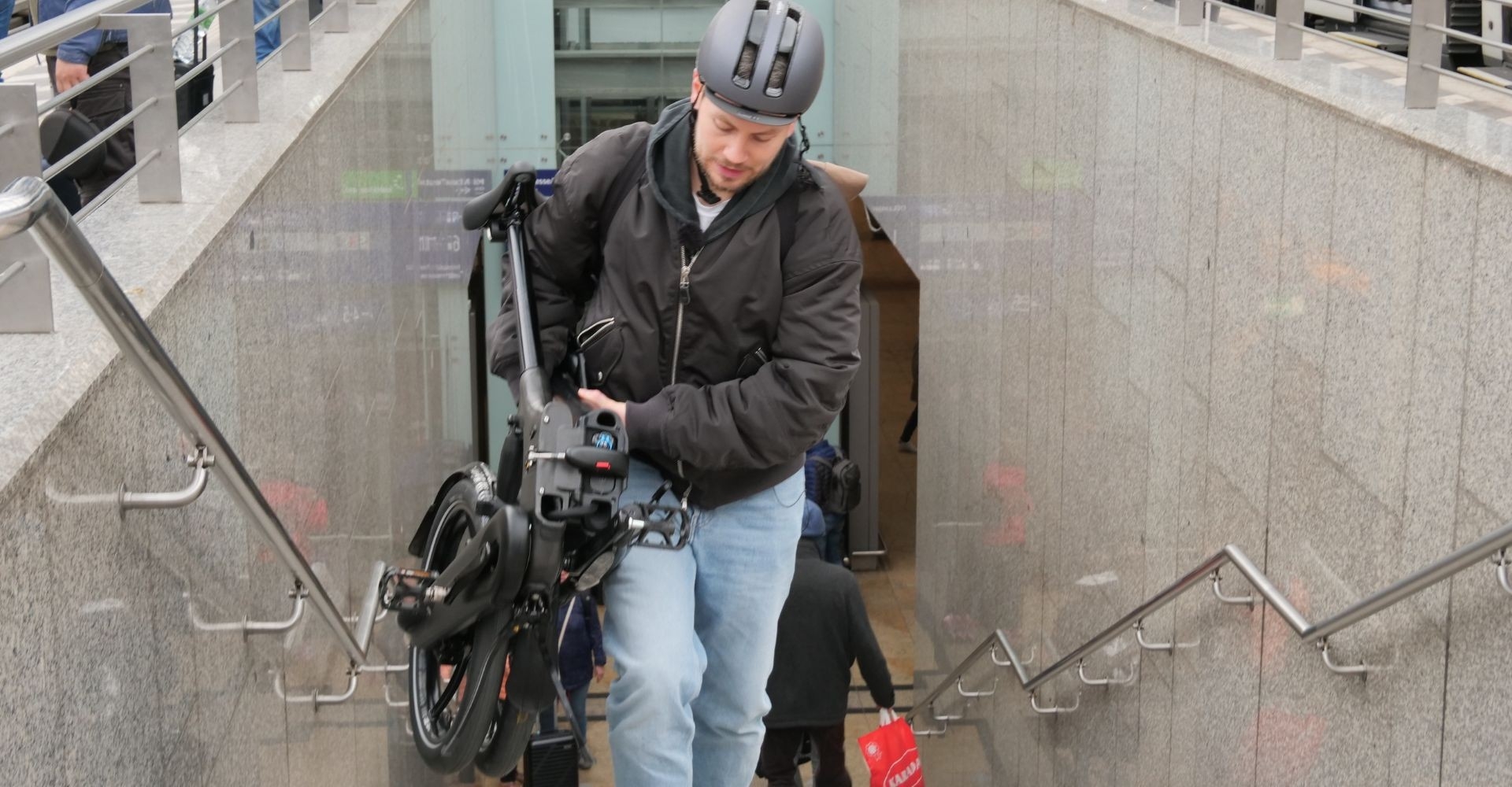 Ein Mann trägt ein Brompton e-Bike Faltrad in Gießen die Treppe hoch, super praktisch in der Stadt.