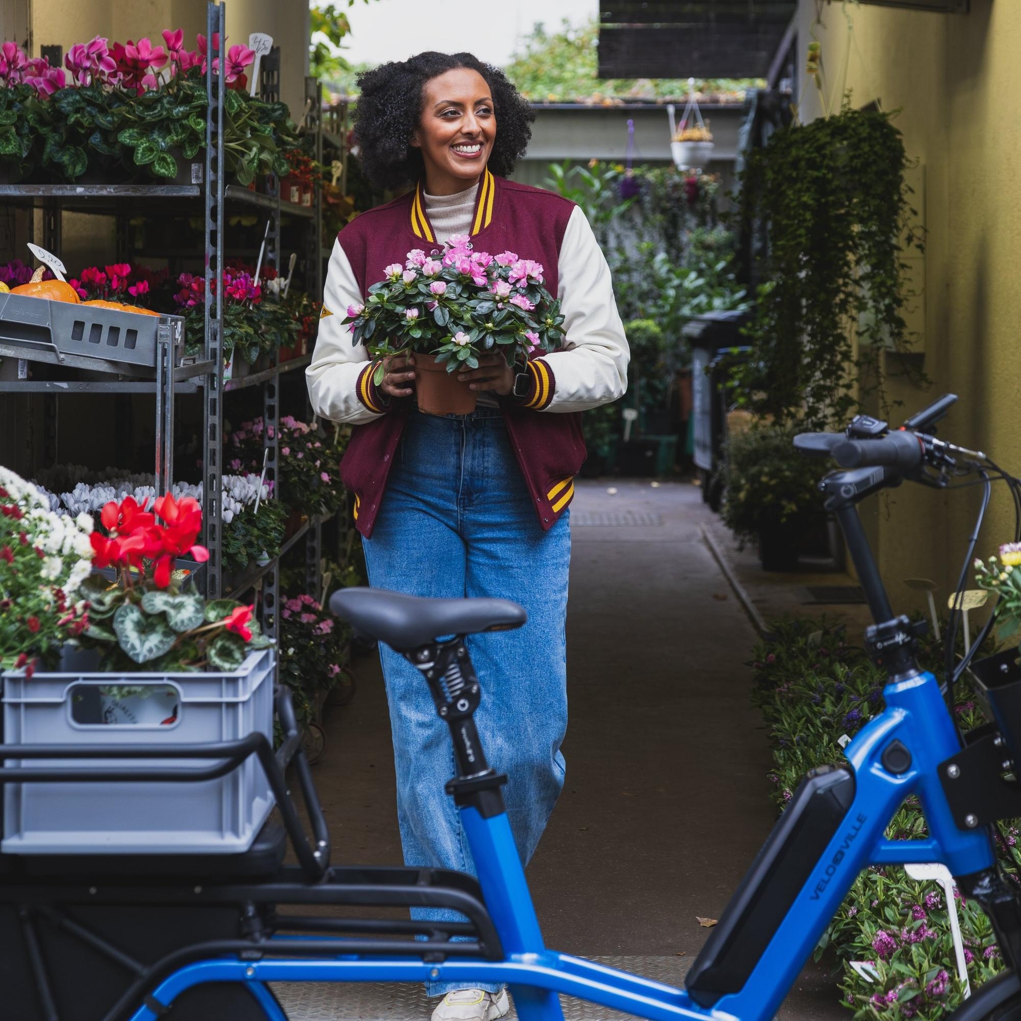 Eine junge Frau steht mit ihrem e-Bike vor einem Blumenladen in Berlin-Mitte und kauft Pflanzen.