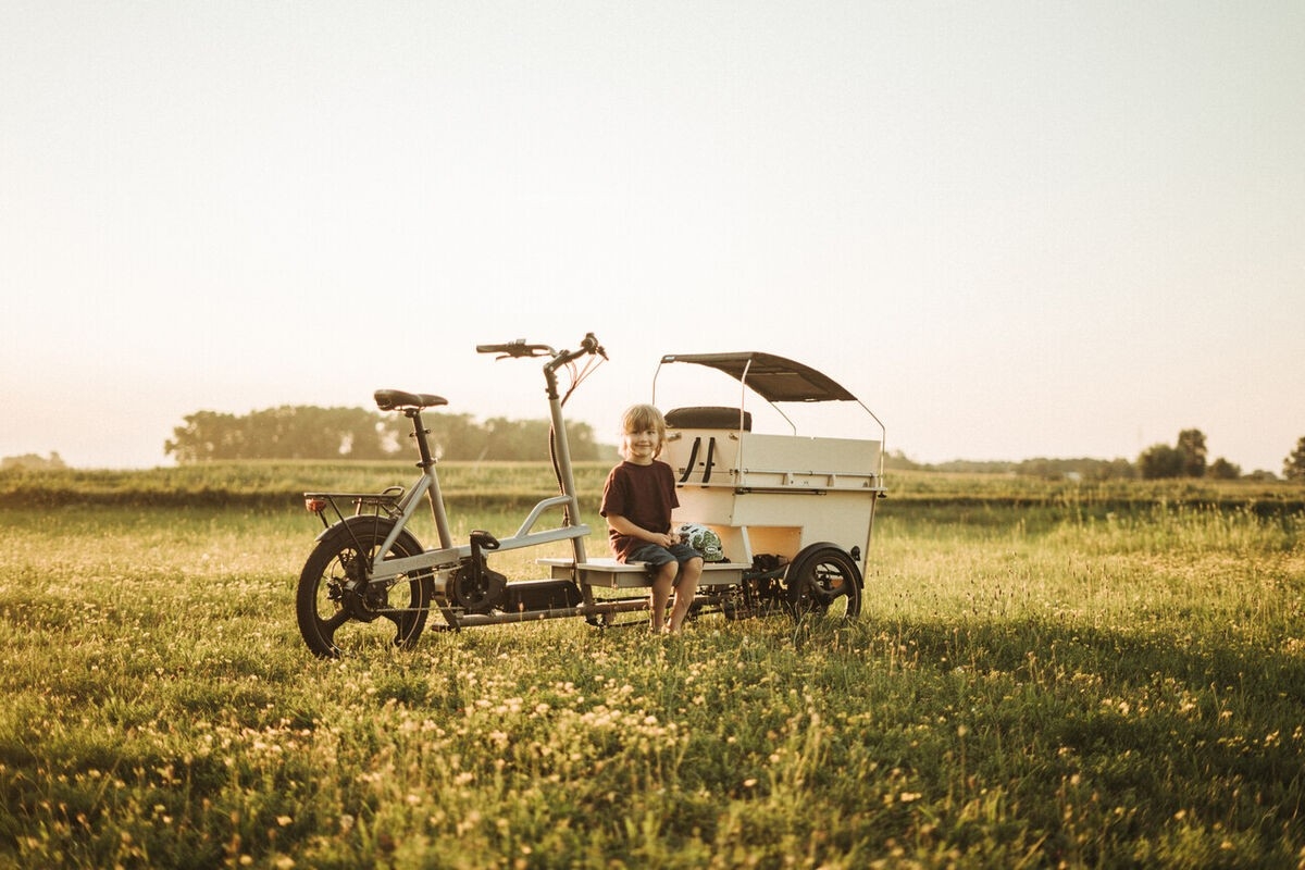Das Bild zeigt ein modernes E-Bike mit einem integrierten Kinderanhänger, auf dem ein Junge sitzt.