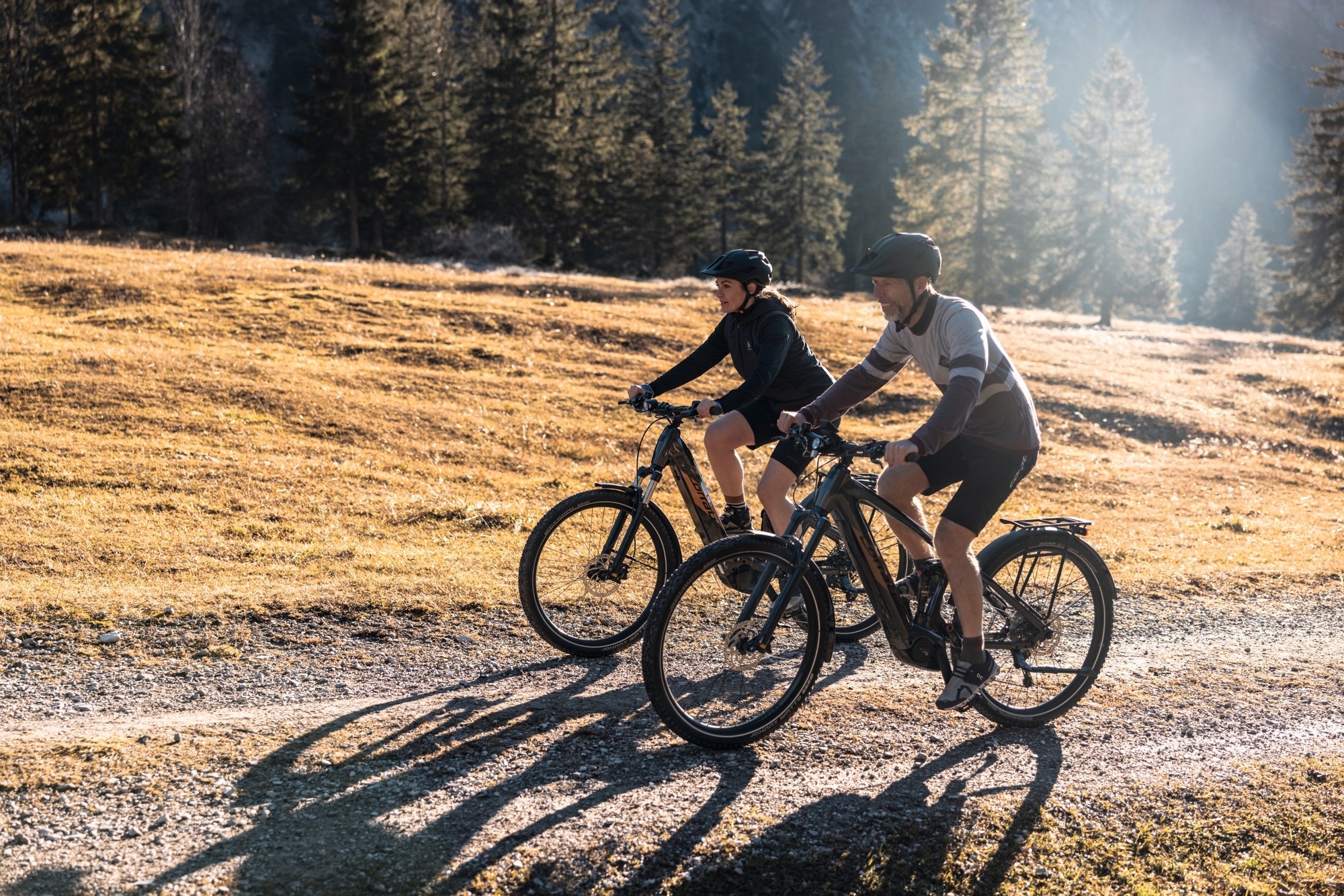 Das Bild zeigt zwei Personen, die auf Trekking E-Bikes durch eine herbstliche Landschaft fahren.