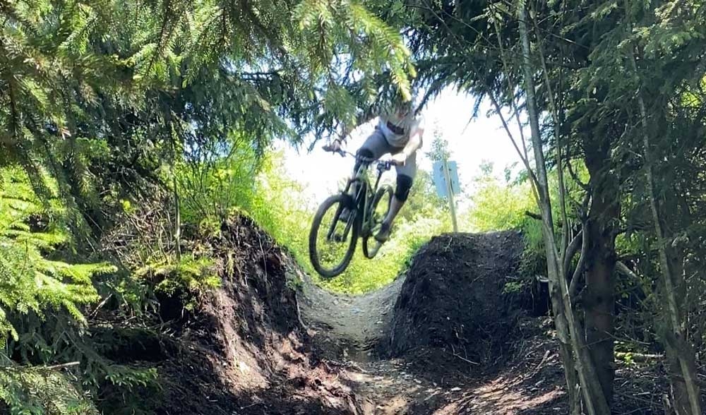 Ein Radfahrer macht einen Sprung auf einem Mountainbike-Pfad durch einen dicht bewachsenen Wald, umgeben von Natur